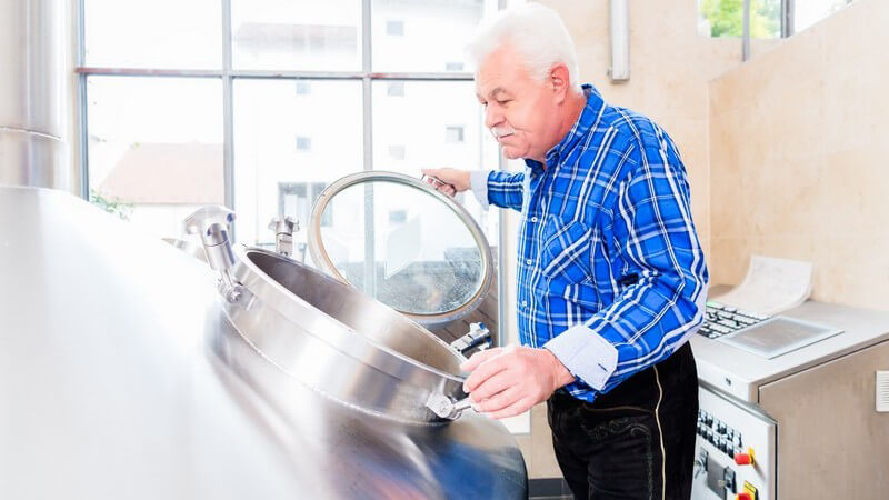 Älterer Braumeister wirft einen Blick in den silbernen Sudkessel einer Brauerei