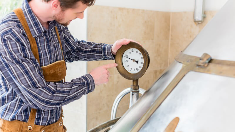 Braumeister in Lederhose steht im Sudhaus einer Brauerei