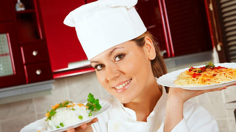 Junge Köchin mit einem Reis- und einem Spaghettiteller in den Händen