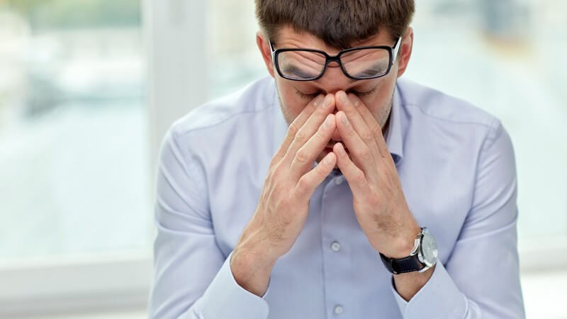 Geschäftsmann in blauem Hemd und mit Brille reibt sich müde die Augen