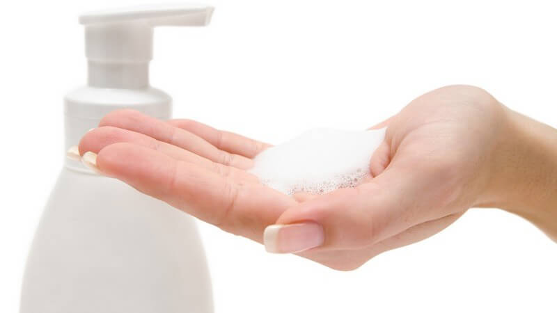 Linke Frauenhand mit Seifenschaum darauf, daneben Seifenspender, weißer Hintergrund