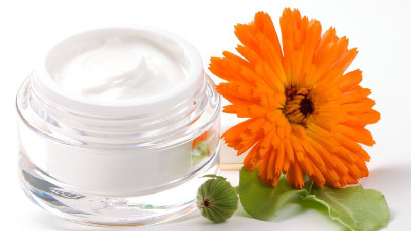 Orangene Calendula Blüte neben Gefäß mit Creme
