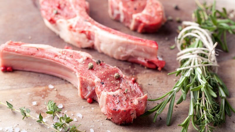 Rohes Hammelfleisch oder Lammkoteletts neben einem Bund Rosmarin