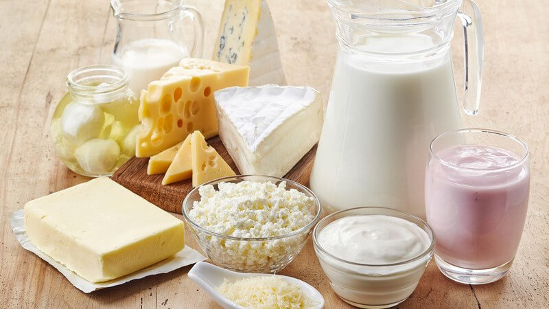 Verschiedene Milchprodukte wie Milch, Butter, Käse, Joghurt und Quark auf einem Holztisch