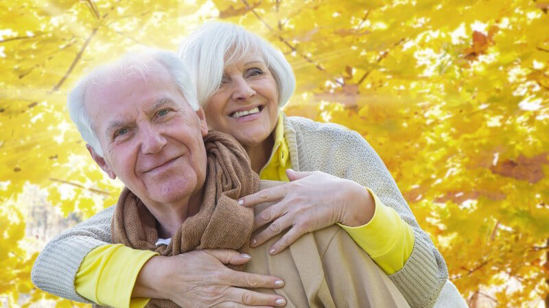 Äteres Paar im Herbst, Spaziergang, sie umarmt ihn von hinten