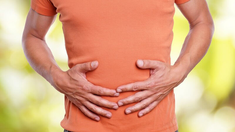 Mann in lachsfarbenem Shirt fasst sich an den Bauch