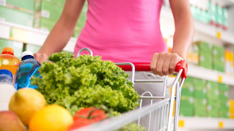 Gesunde Ernährung - Frau mit vollem Einkaufswagen mit Gemüse und Obst im Supermarkt