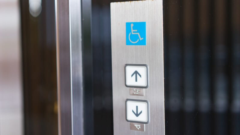 Blaues Behindertenzeichen (Rollstuhlsymbol) über den Hoch-/Runtertasten in einem Aufzug