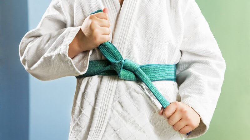 Junge im Judoanzug knotet grünen Judogurt zusammen