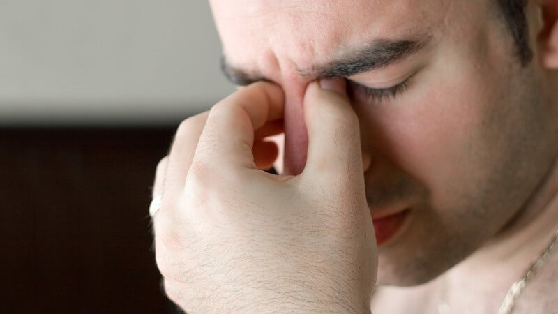 Erschöpfter Mann mit geschlossenen Augen fasst sich ins Gesicht