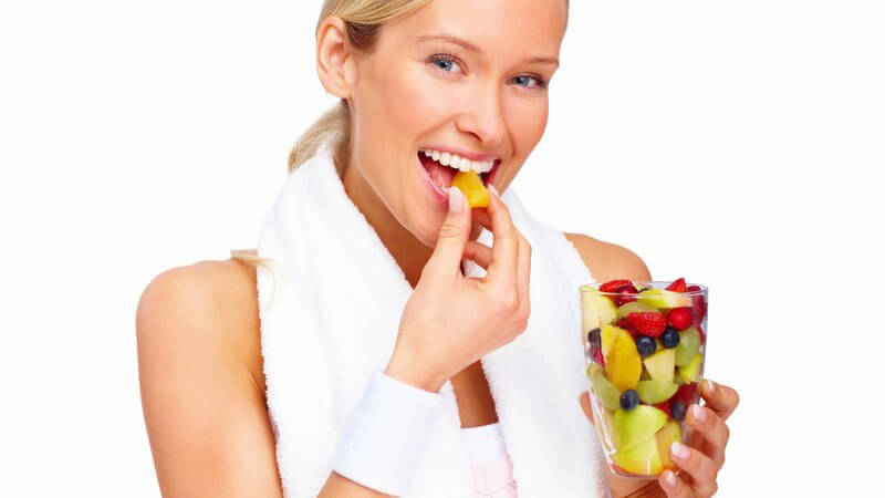 Junge Frau mit Handtuch um Schulter isst Obstsalat aus Becher