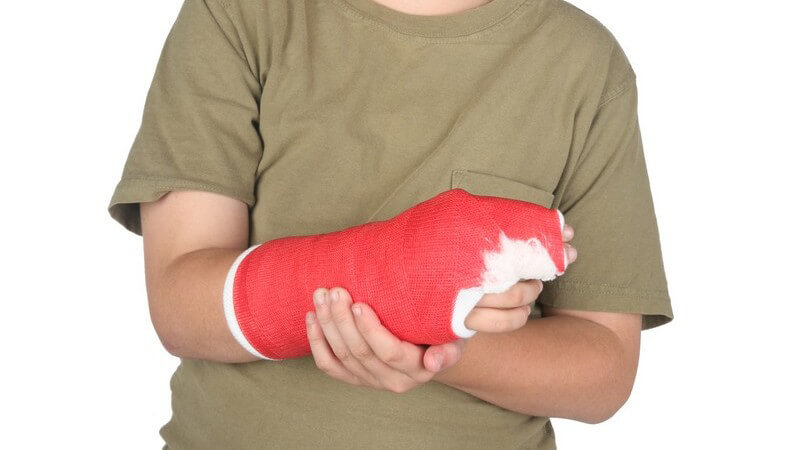 Kleiner Junge trägt rechten Arm in Gips, weißer Hintergrund