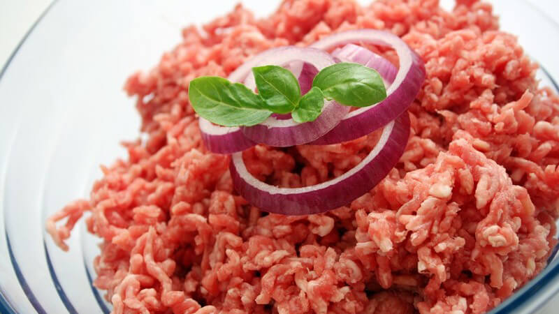 Rohes Hackfleisch in Glasschale, garniert mit Zwiebelringen und Basilikum