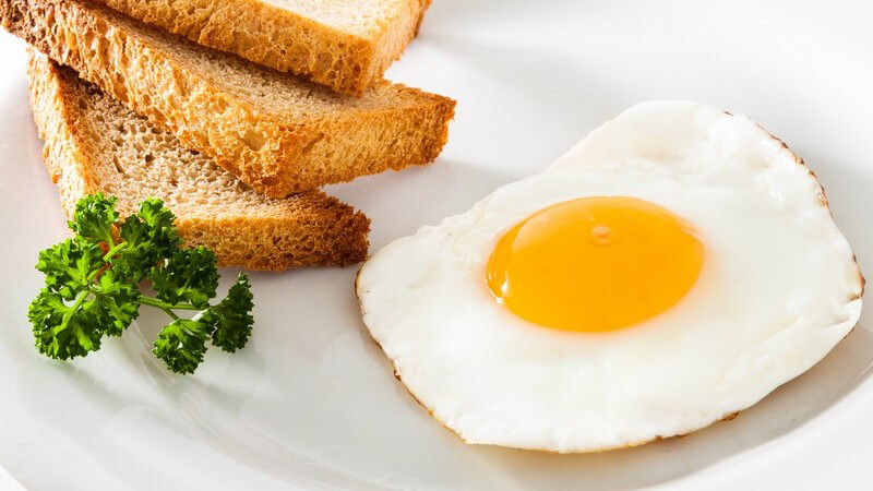 Drei Toastecken neben Spiegelei und Petersilie auf weißem Teller