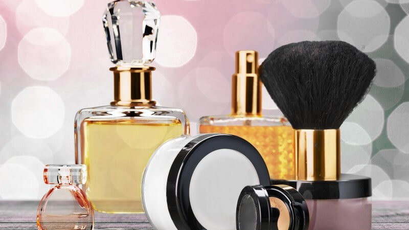 Parfümflakons und Make-up vor glitzerndem Hintergrund