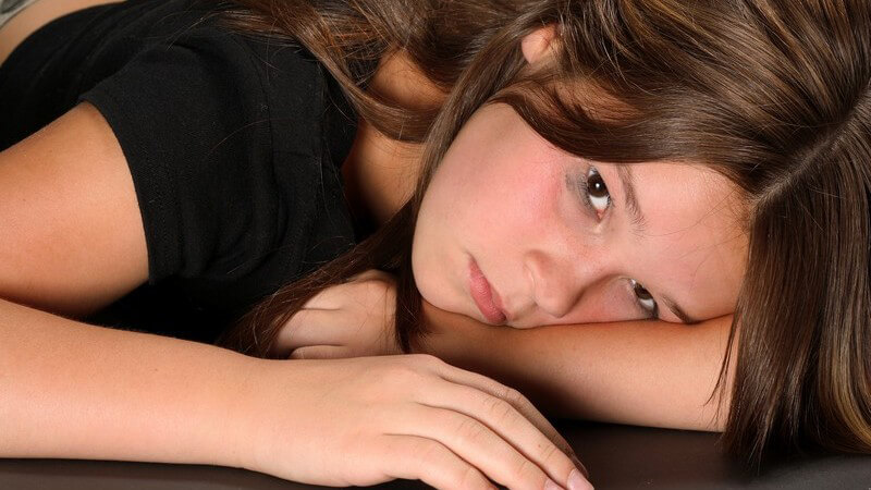 Junges Mädchen liegt traurig mit verweinten Augen auf dem Boden