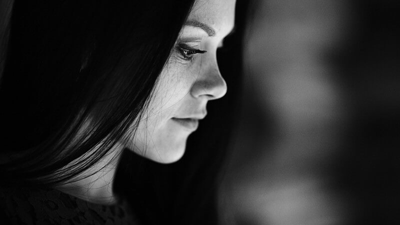 Dunkles Portrait einer Frau mit langen schwarzen Haaren, guckt traurig