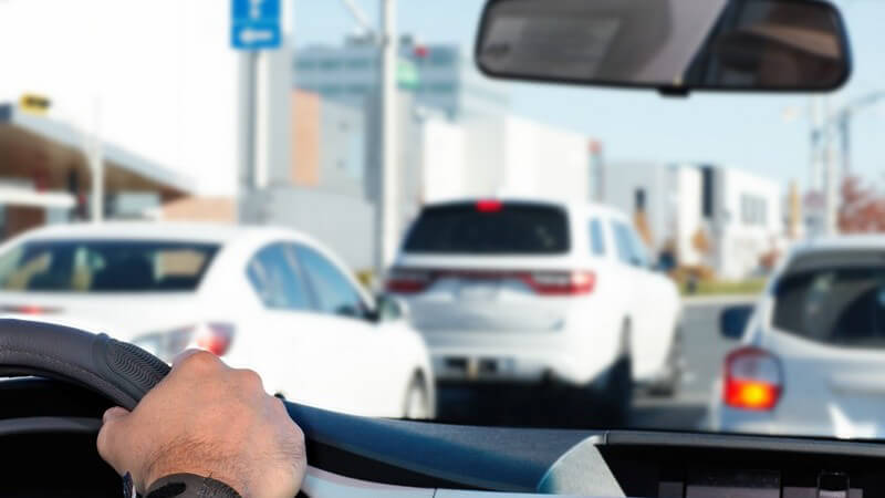 Blick aus der Frontscheibe eines Autos, Hand am Lenker, drei Autos voraus
