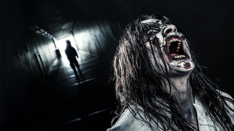 Schreiende Zombie-Frau mit langen schwarzen Haaren am Ende eines dunklen Tunnels