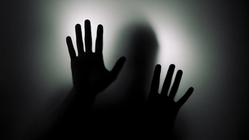 Milchige Glasscheibe, dahinter Schatten eines Mannes, Hände auf Scheibe