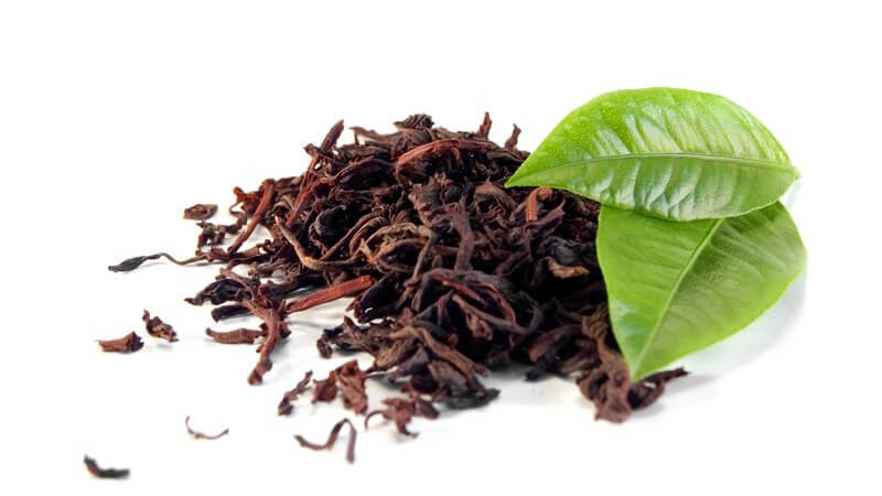 Getrockneter Tee, daneben zwei grüne Blätter auf weißem Hintergrund