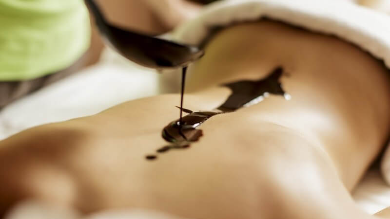 Frau wird bei einer Schokoladenmassage flüssige Schokolade mit einer flachen Kelle auf den Rücken gegossen