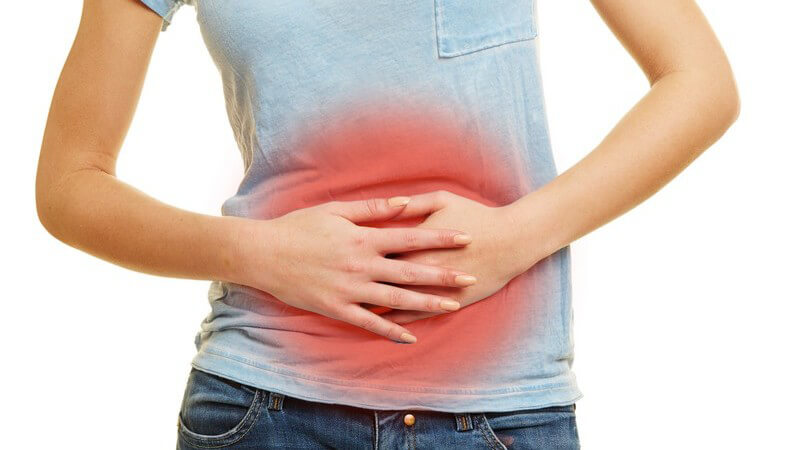 Frau in Jeans und blauem Shirt hat Bauchschmerzen und Magenkrämpfe, Bauchraum rot hervorgehoben