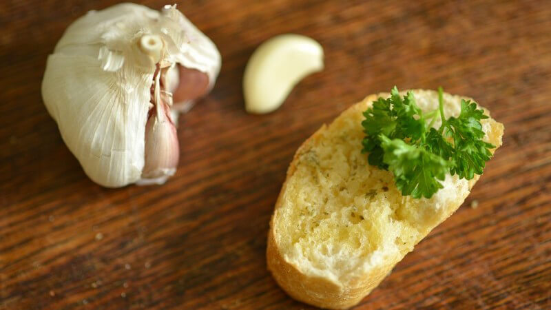 Knoblauchbrot mit Petersilie neben Knoblauchzehe und -knolle