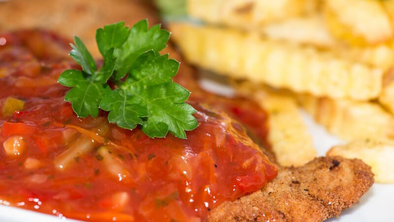 Nahaufnahme eines Schnitzels mit Zigeunersauce, im Hintergrund Pommes frites