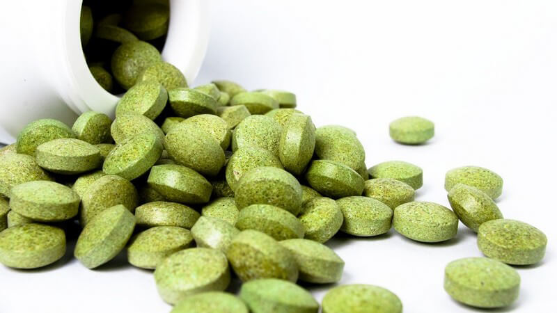 Grüne Pillen, die aus einer weißen Flasche kullern