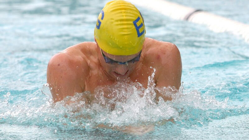 Mann mit gelber Badekappe und blauer Schwimmbrille beim Brustschwimmen