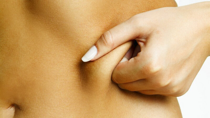 Sportliche in Unterwäsche Frau kneift sich in ihren Bauch