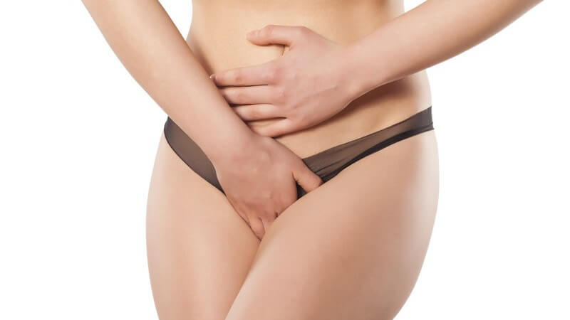 Frau in schwarzem Slip fasst sich an Unterleib und Intimbereich