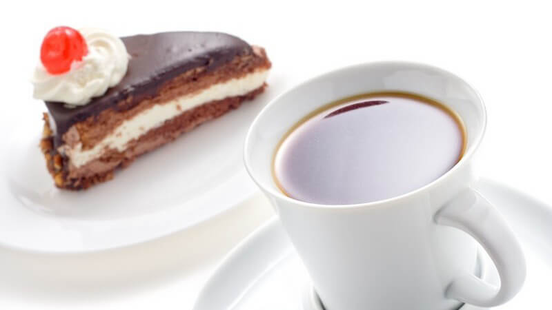 Eine Tasse Kaffee neben Stück Schokoladentorte auf weißem Hintergrund