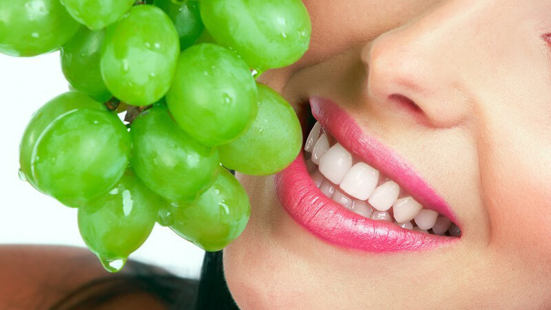 Frau mit pinkem Lippenstift hält frische grüne Trauben an ihren Mund