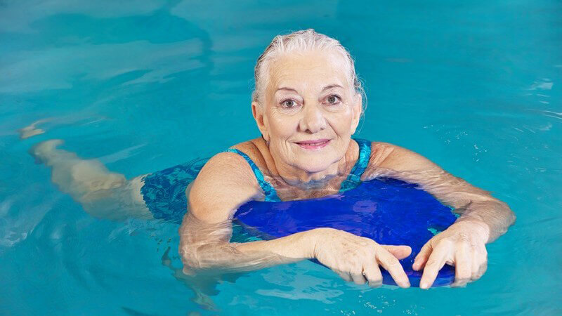 Seniorin beim Schwimmen mit einem blauen Schwimmbrett