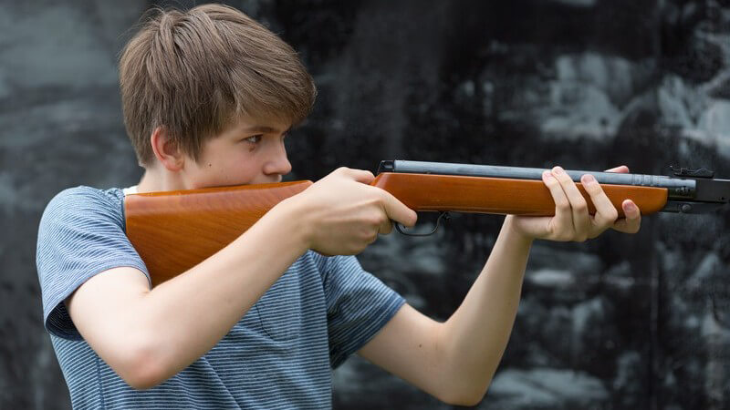 Jugendlicher hat Gewehr angelegt und zielt auf etwas