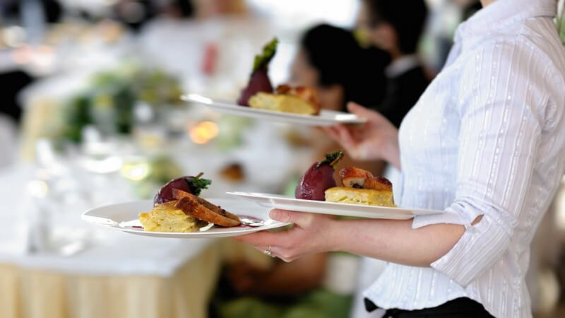 Kellnerin im Restaurant trägt drei Teller mit Speisen