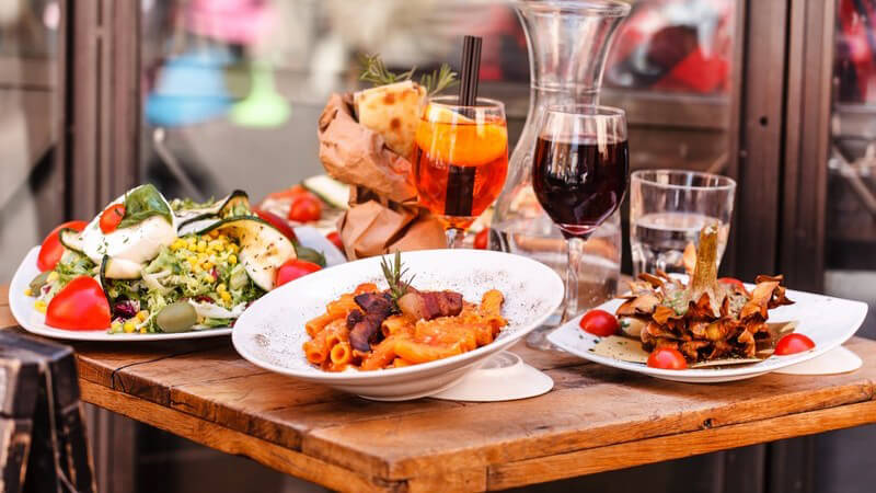 Italienische Speisen auf Holztisch im Restaurant - Salat, Pasta und Wein