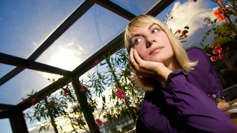 Junge Frau sitzt im Restaurant im Wintergarten und hat Kopf nachdenklich auf Hand gestützt