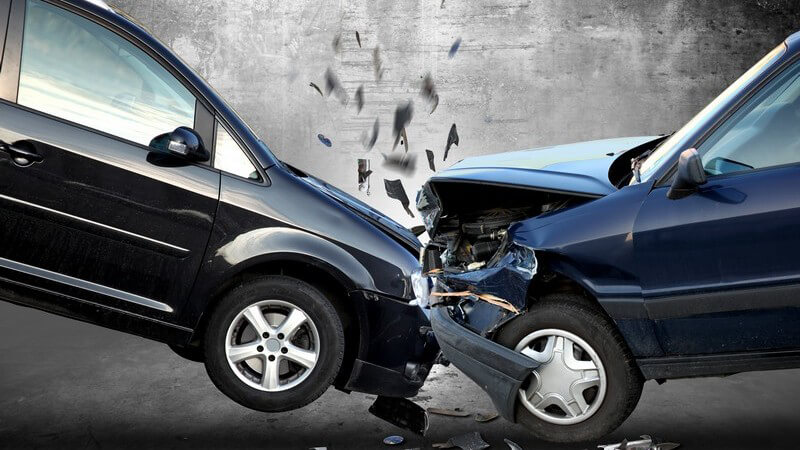 Unfall zwischen einem schwarzen und blauen Auto vor einer grauen Wand