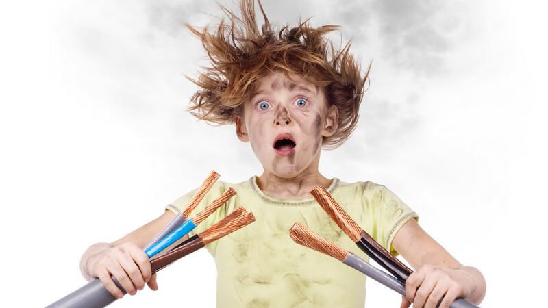 Kleiner Junge mit verrusten Haaren und Gesicht, hält Kabelenden in Händen, Stromschlag