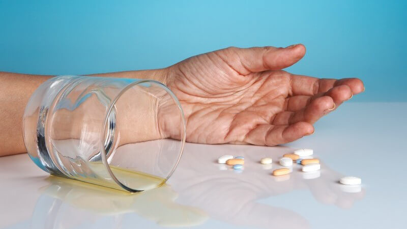 Umgekipptes Glas mit Alkohol, mehrere Tabletten, ein liegender Arm, Selbstmord
