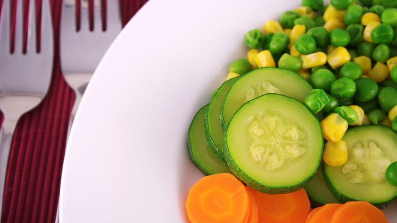 Frisches Gemüse in weißem Teller, daneben zwei Gabeln