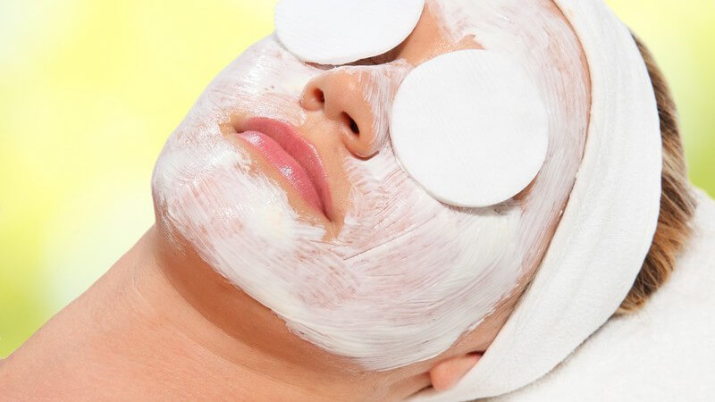 Frau mit weißer Gesichtsmaske, Stirnband und Wattepads auf den Augen