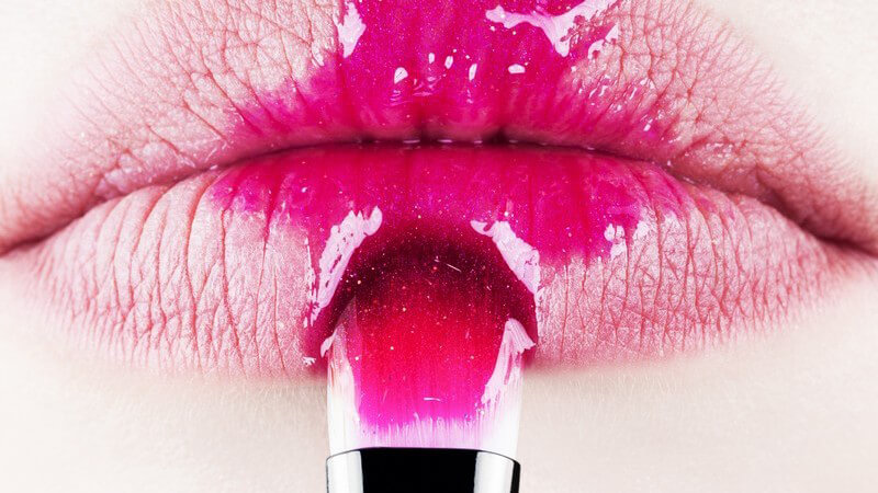 Weiblicher Mund in Nahaufnahme mit pinkem Lipgloss und Pinselspitze an der Unterlippe