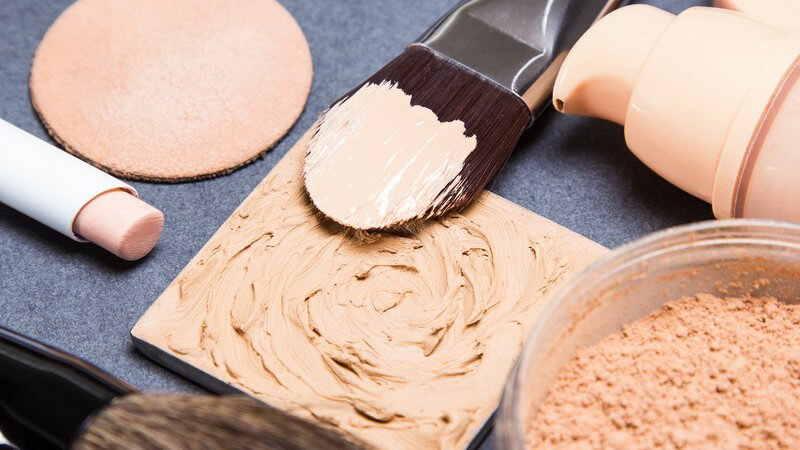 Pinsel liegt auf angemischtem hautfarbenen Make-up, daneben ein Make-up-Pad und -Stift