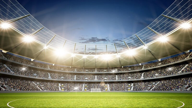 Blick von der Mittellinie ins hellbeleuchtete Stadion mit grünem Rasen