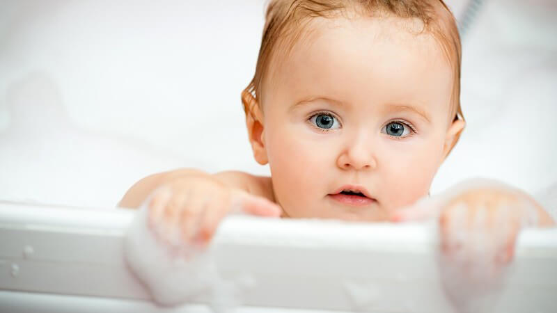 Baby guckt aus einer Badewanne voller Schaum
