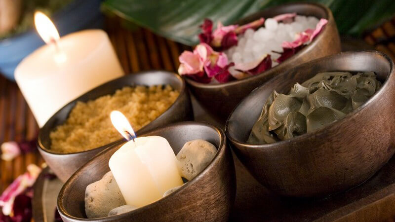 Wellness - Vier braune Gefäße mit Wellnesszutaten und Kerzen